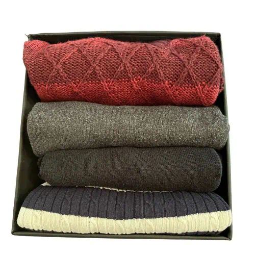 four folded sweaters in a black box on a white background, with one folded and the other folded