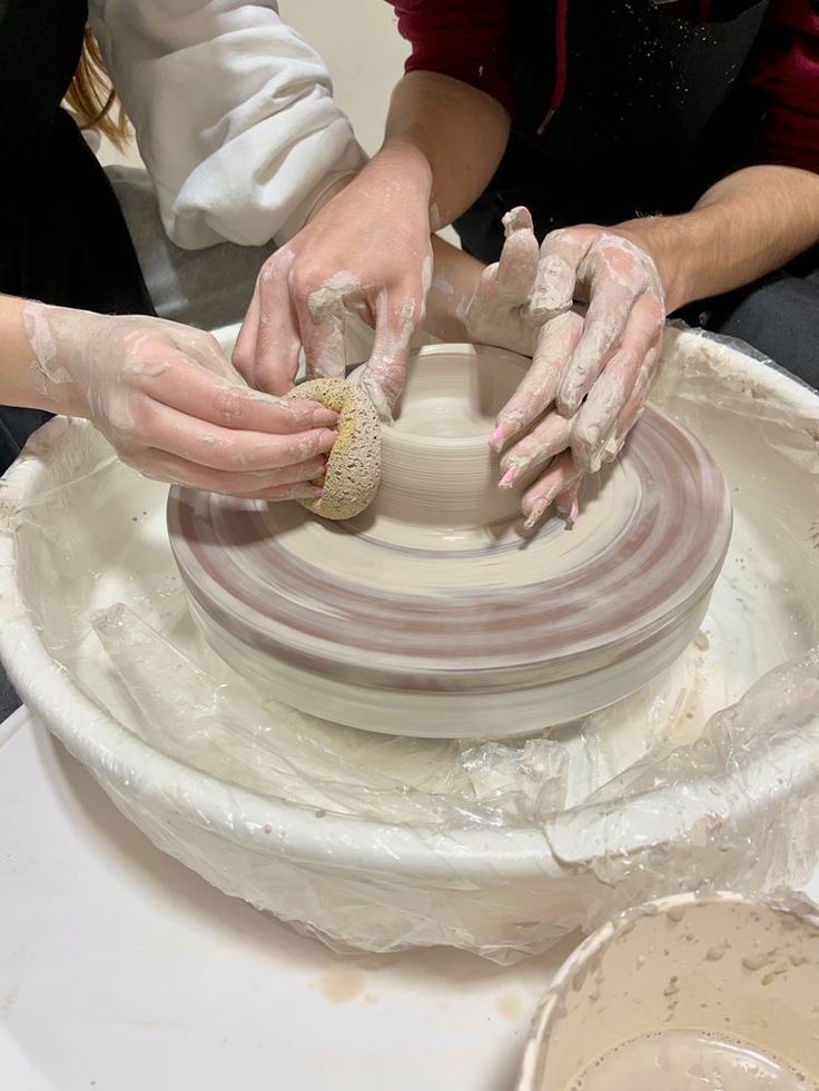 two people making pottery on a potter's wheel with their hands in the process