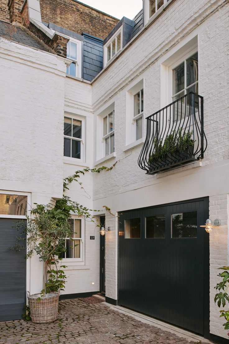 a white brick building with a black garage door and planter on the top floor