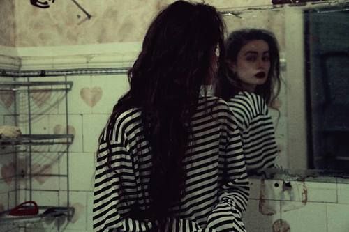 a woman with long hair standing in front of a bathroom mirror looking at her reflection