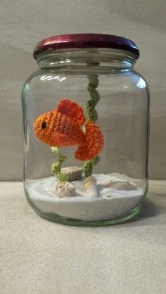 an orange fish in a glass jar filled with sand