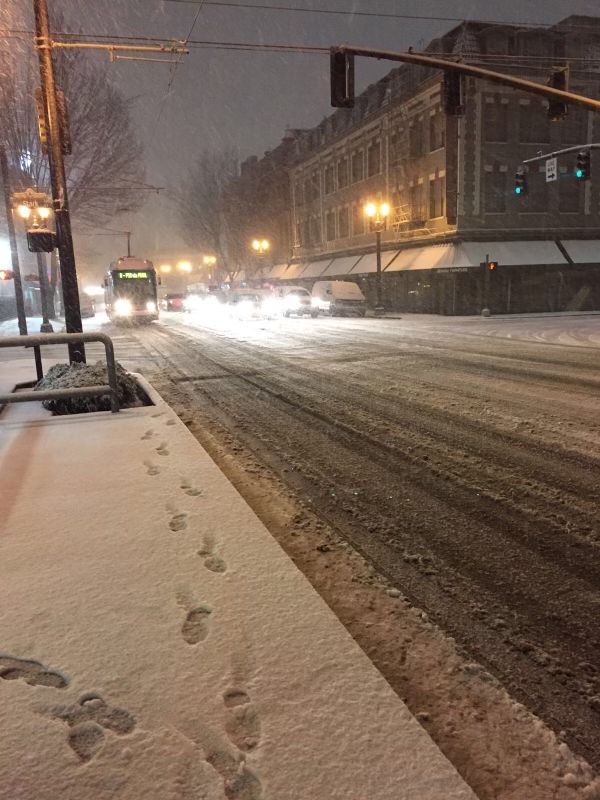 a snowy street with tracks in the snow next to traffic lights and cars driving down it