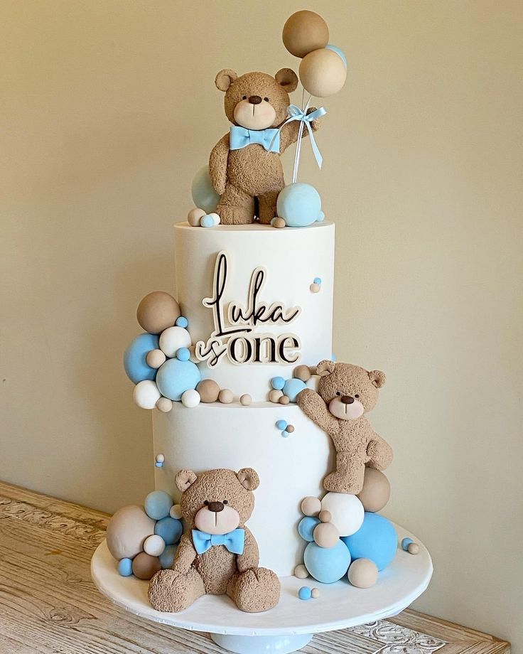 a three tiered cake with teddy bears on top and balloons in the shape of letters