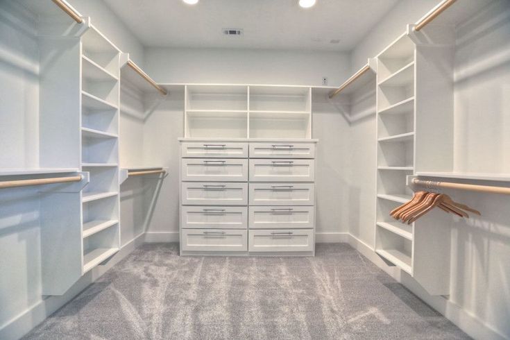 an empty walk in closet with white shelves and drawers