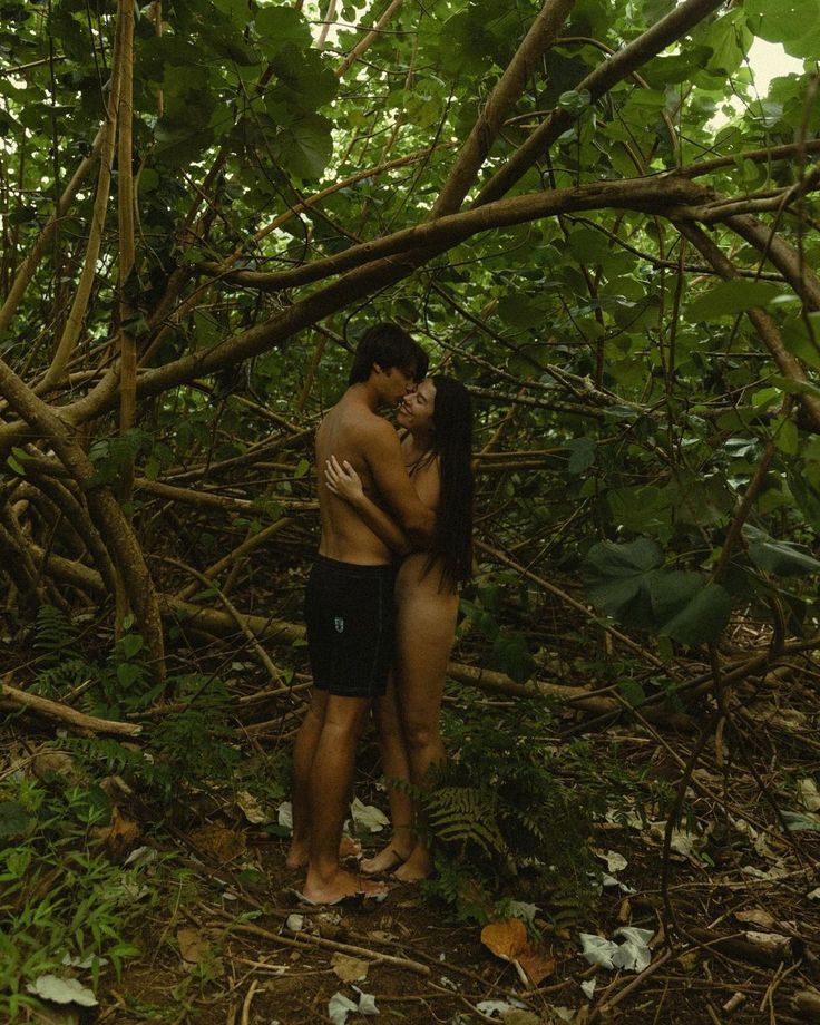 two people standing in the woods hugging each other