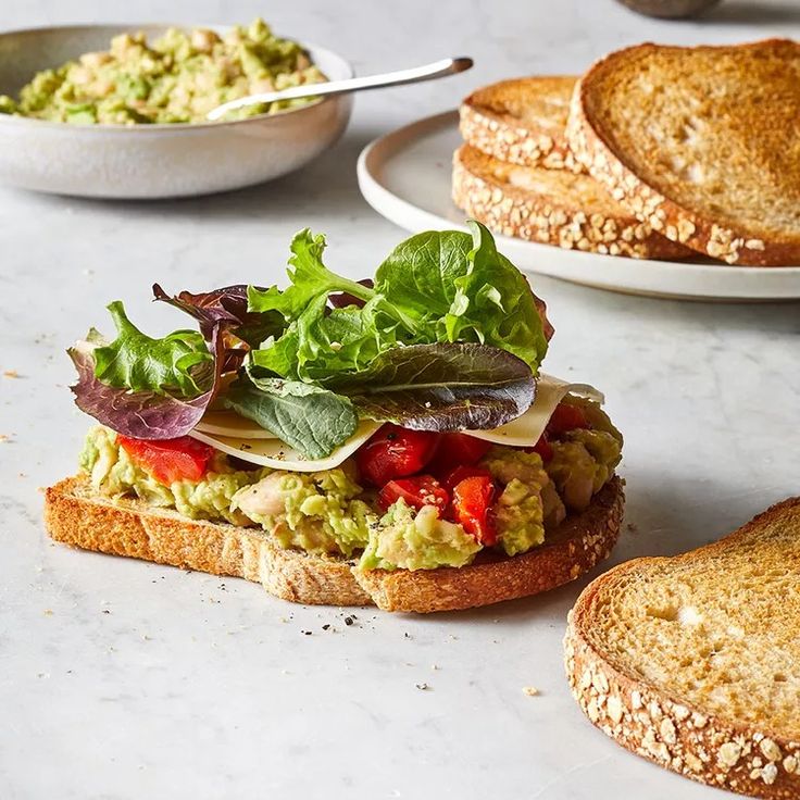 an open face sandwich with lettuce, tomato and avocado on it