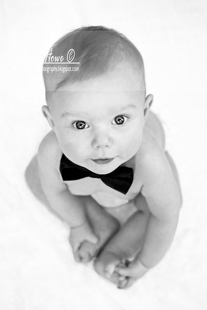 a baby wearing a bow tie laying on top of a white blanket in black and white