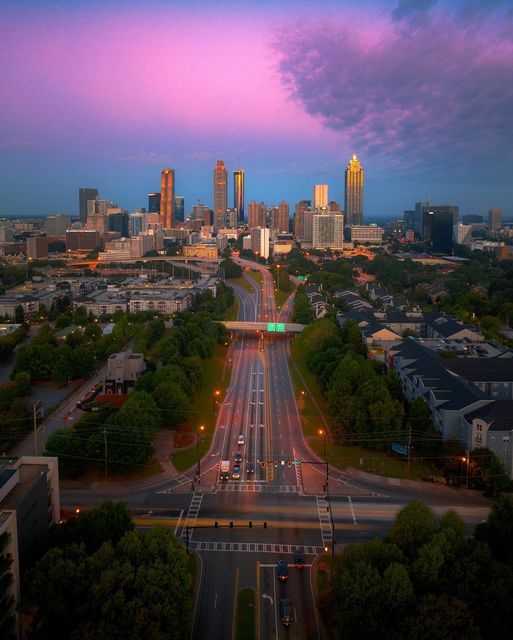 an aerial view of a city at dusk with cars driving on the road and buildings in the background