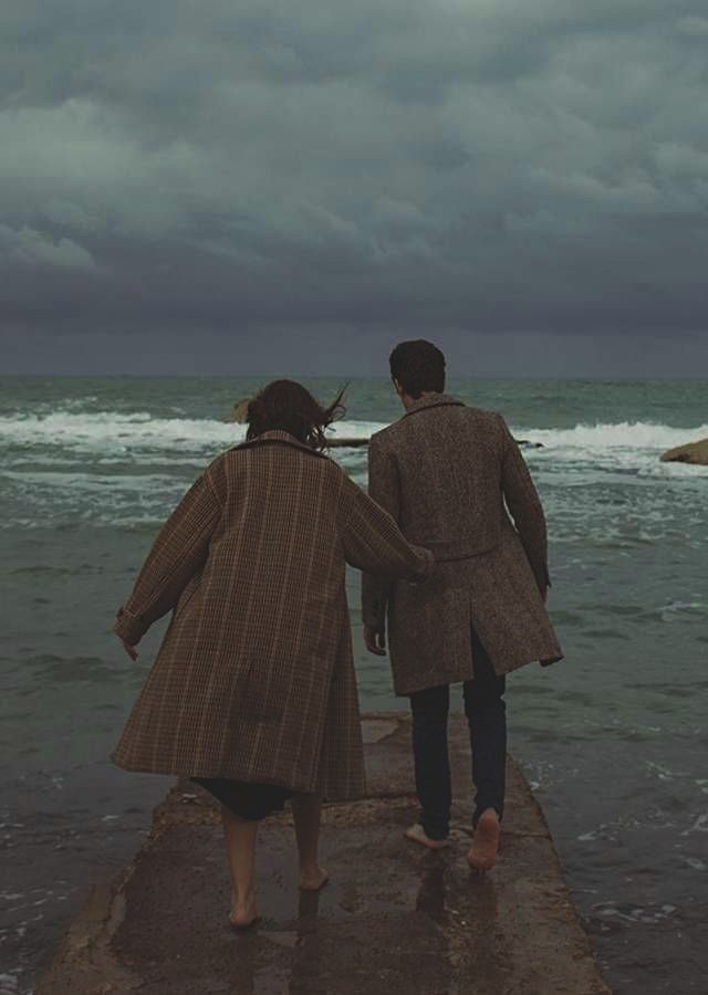 two people are walking along the beach in the rain and dark clouds over the ocean