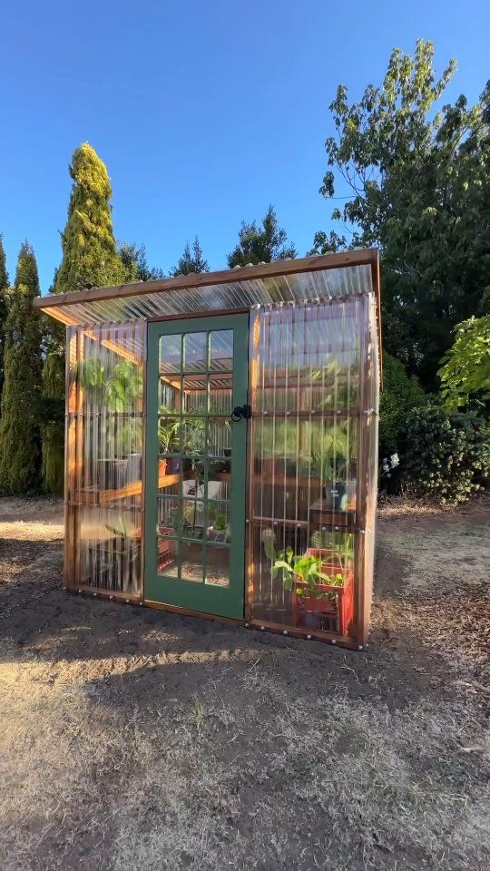 a small greenhouse in the middle of a field with lots of plants growing out of it