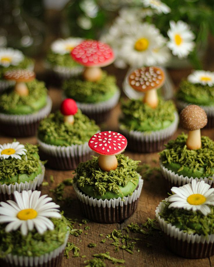 cupcakes decorated with moss, mushrooms and daisies are on a table next to flowers