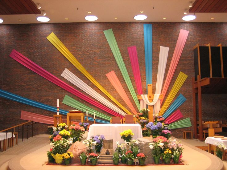 a church decorated with colorful ribbons and flowers on the alter, in front of a brick wall