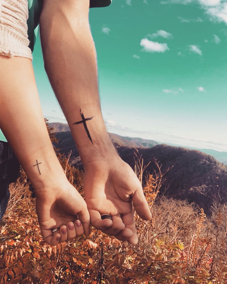 two people holding hands with cross tattoos on their wrists and the sky in the background