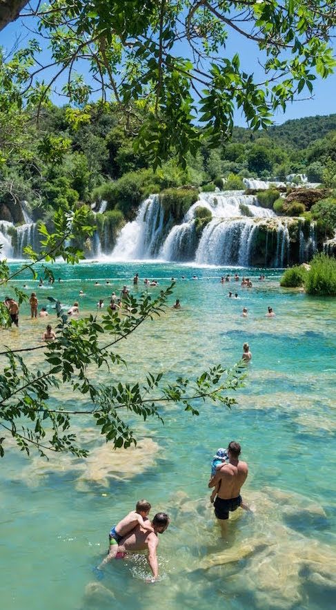 people are swimming in the water near a waterfall