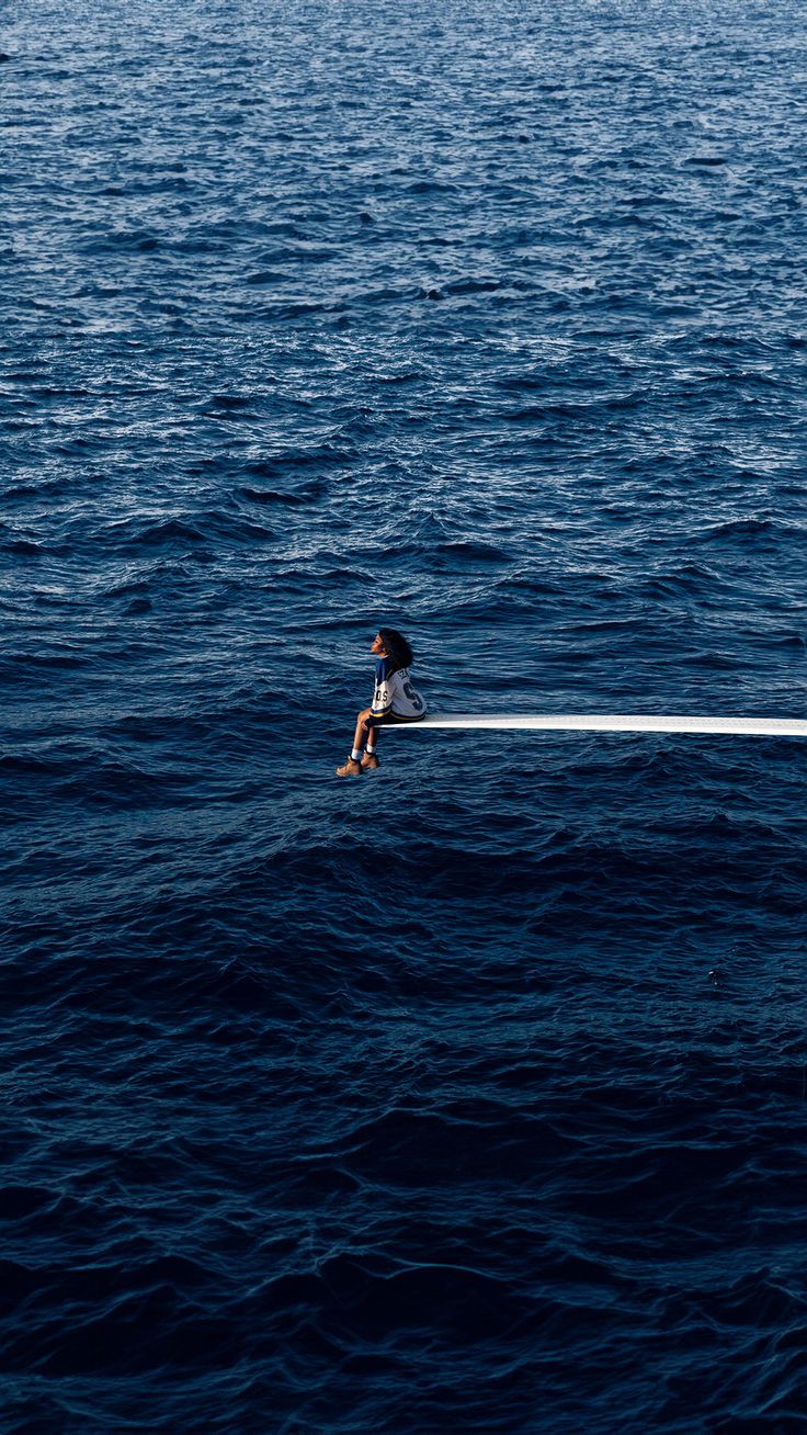 a person sitting on top of a boat in the middle of the ocean with their legs crossed