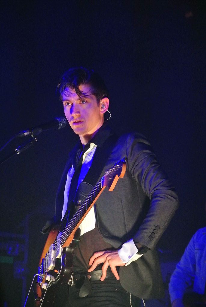 a man in a tuxedo playing an acoustic guitar on stage at a concert