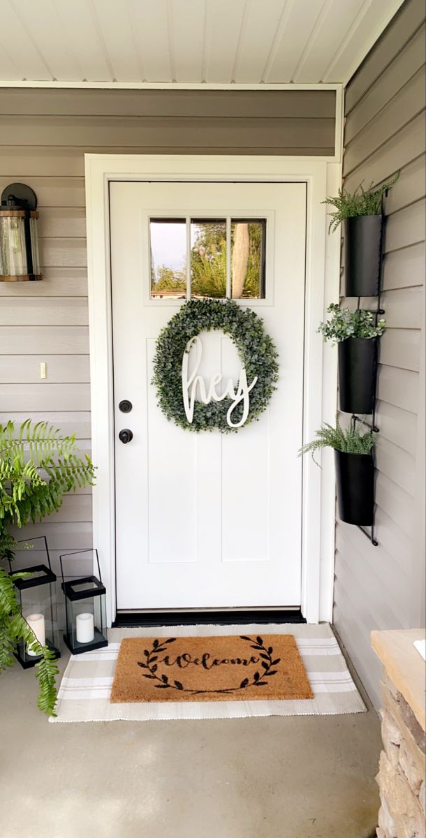 a white door with a wreath on it and some black planters next to it