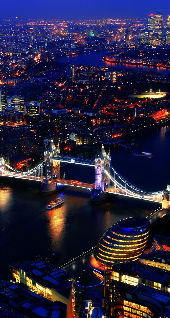 an aerial view of london at night with the tower bridge lit up in red and blue