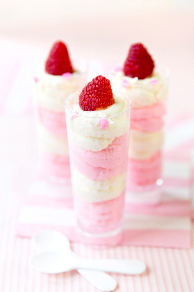 three small desserts with strawberries in them on a pink and white tablecloth