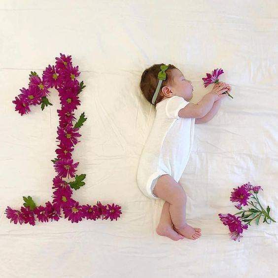 a baby laying on top of a bed next to purple flowers and the letter e