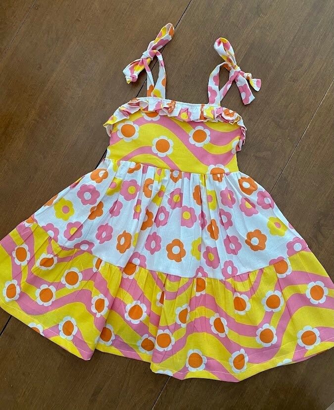 Twirl into spring and summer in this groovy daisy sundress. Made from comfortable cotton it has shoulder ties and an elastic back for that perfect fit. Cotton Mini Sundress With Tie Straps, Cotton Sundress With Tie Straps In Mini Length, Cotton Sundress With Tie Straps, Mini Length, Playful Floral Print Sundress For Summer, Playful Floral Sundress For Summer, Summer Cotton Sundress With Adjustable Straps, Cotton Sundress With Adjustable Straps For Summer, Spring Sundress With Tie Straps For Day Out, Playful Sleeveless Dress With Tie Straps