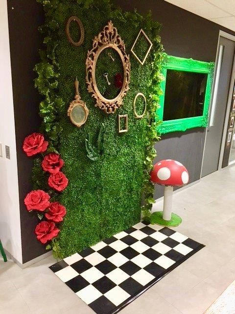 a green wall covered in moss and red flowers next to a black and white checkered floor