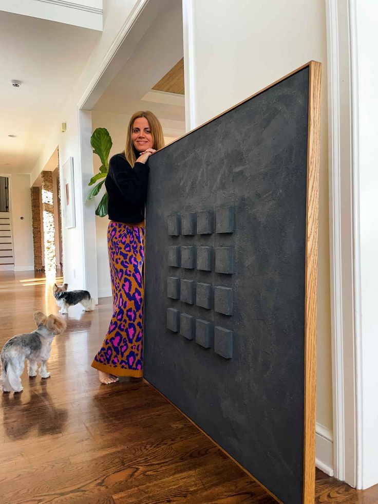 a woman standing next to a large black board on top of a hard wood floor