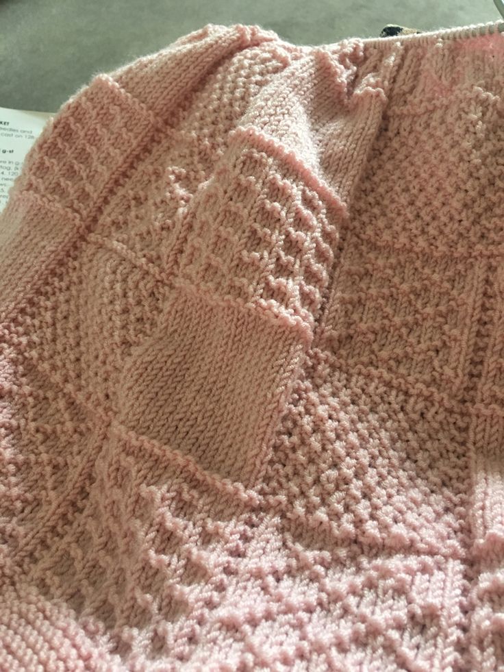 a pink knitted blanket sitting on top of a table next to an open book