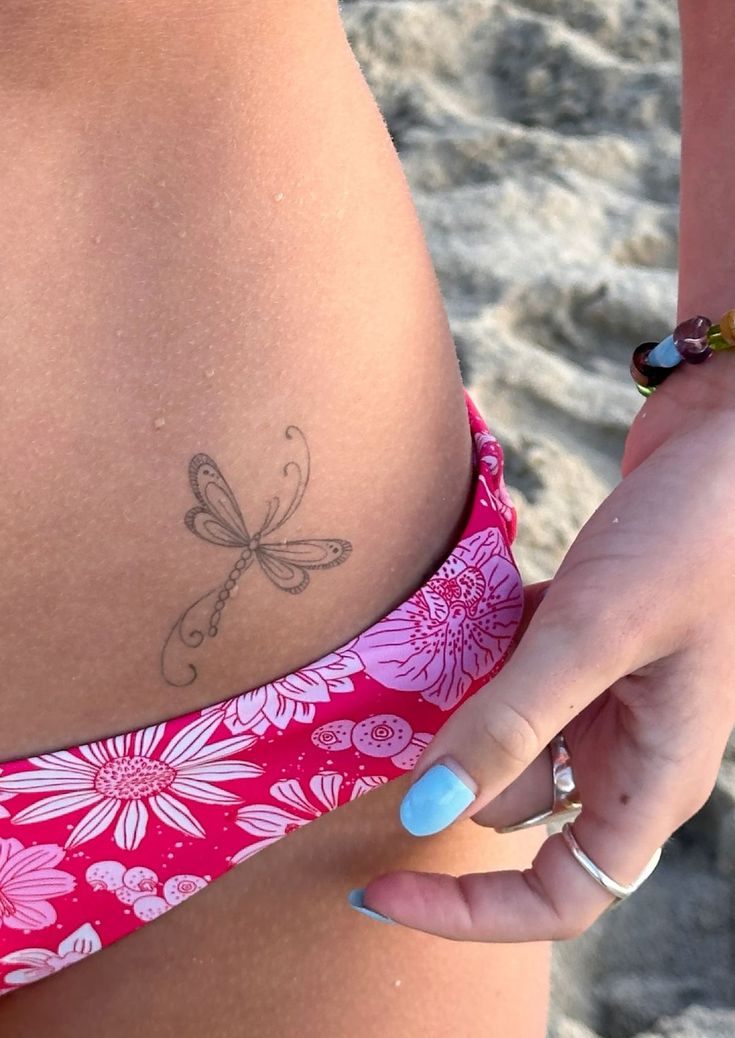 a woman with a dragonfly tattoo on her stomach is standing in front of the ocean