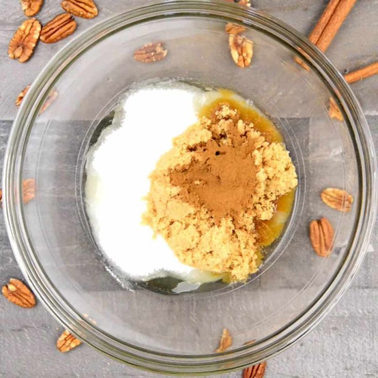 a glass bowl filled with some food on top of a wooden table next to pecans