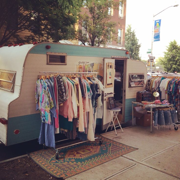 an old camper trailer with clothes hanging from it's rack and other items on display