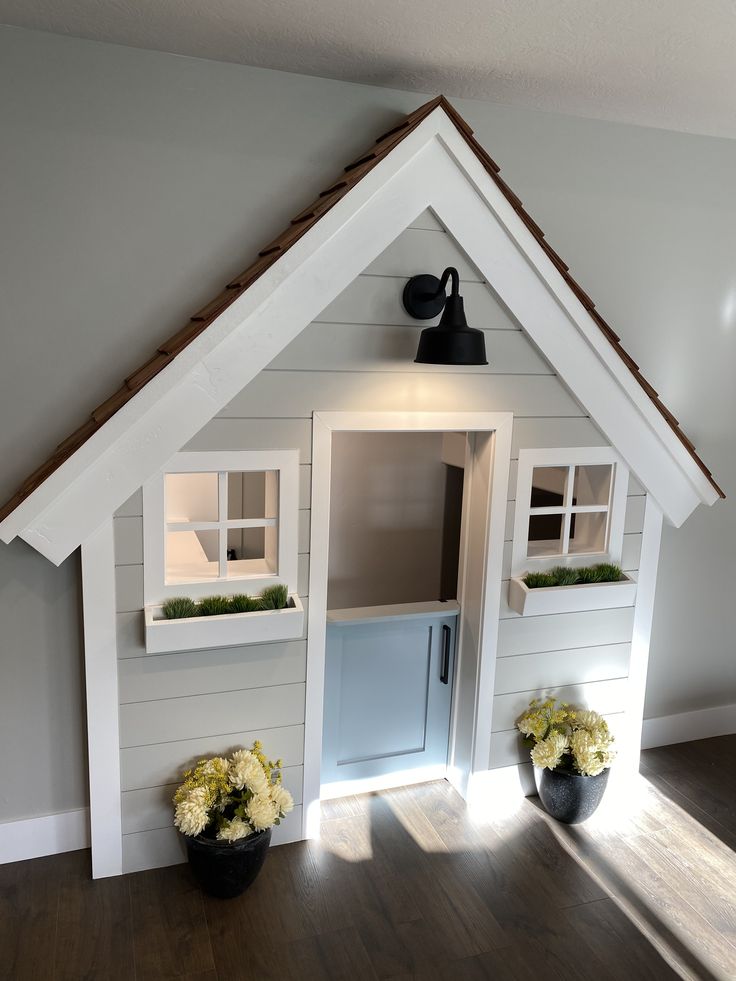 there is a dog house made out of wood and white sidings with flowers in the window boxes