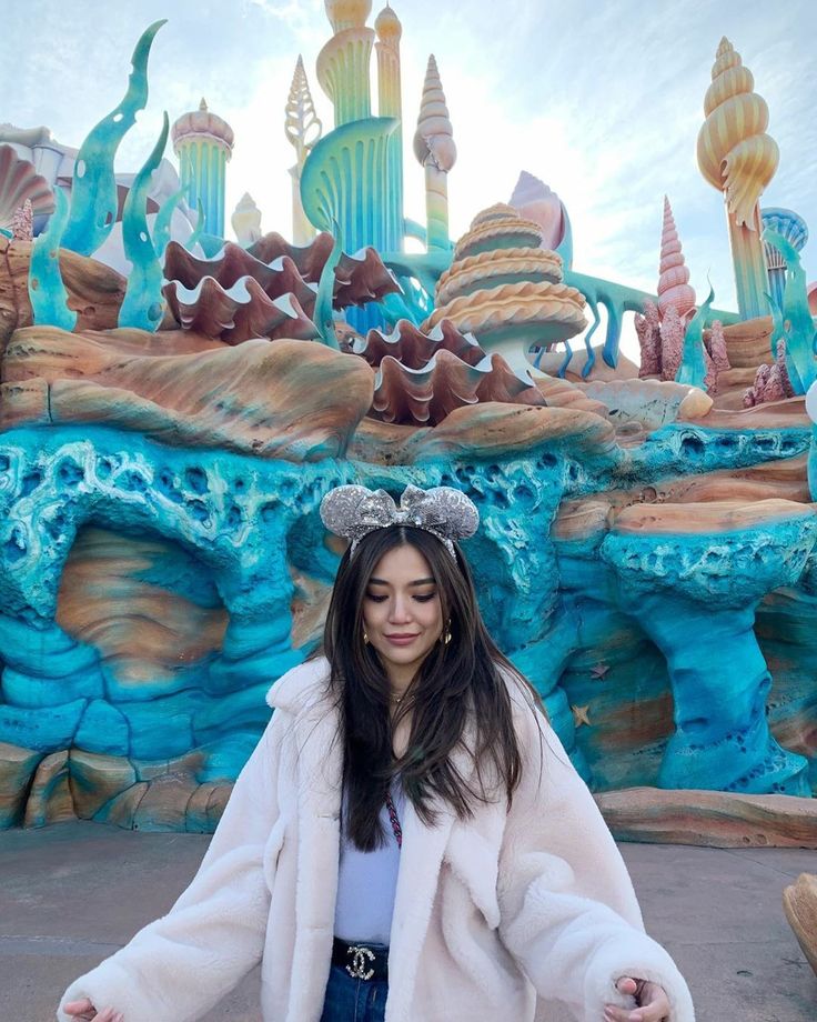 a woman standing in front of a blue and green theme park with her arms outstretched