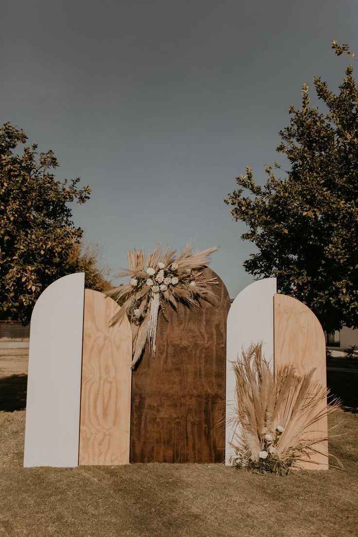 an outdoor wedding ceremony setup with tall grass and flowers on the back of two large wooden boards