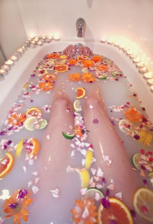 a bathtub filled with lots of oranges and other things on the floor in front of a window