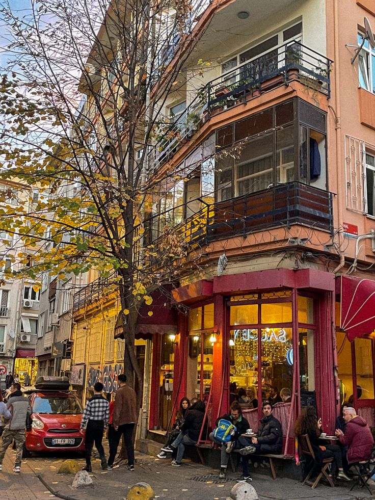 people are sitting outside on the sidewalk in front of a building with red awnings