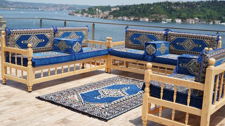 a wooden patio with blue cushions and rugs on it's deck overlooking the water