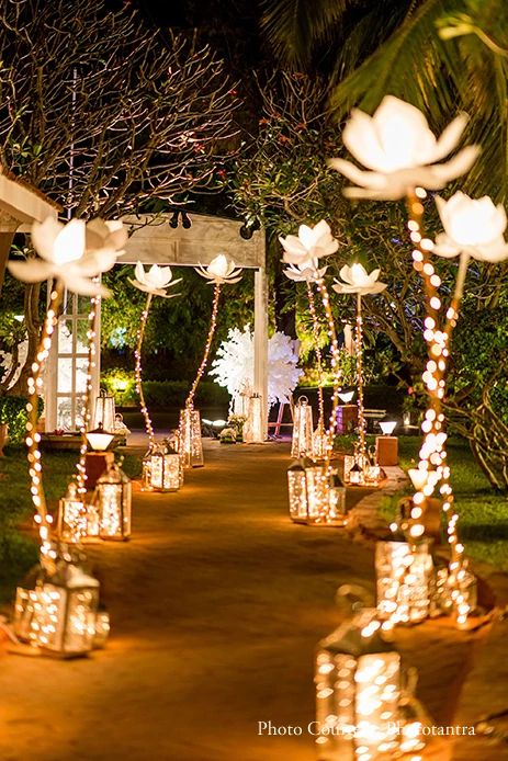 lighted lanterns are lined up on the path to an outdoor ceremony venue at night time