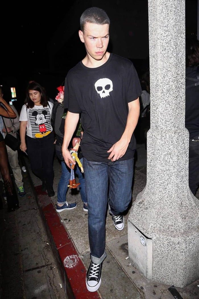 a young man standing on the sidewalk with his hands in his pockets and wearing black converse shoes