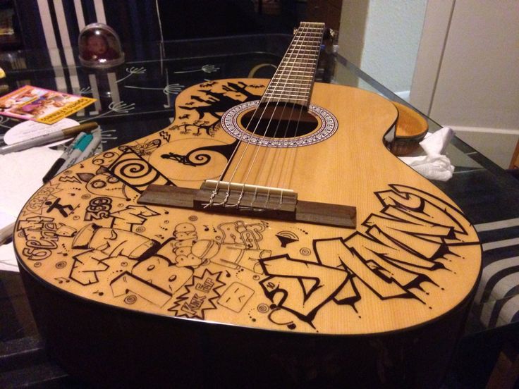 a wooden guitar with graffiti on it sitting on top of a glass table in front of a mirror