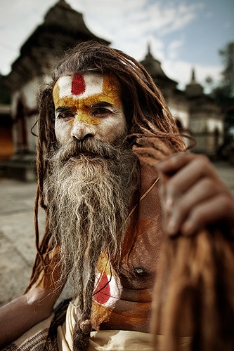 a man with long hair and white face paint on his face is sitting in front of a building