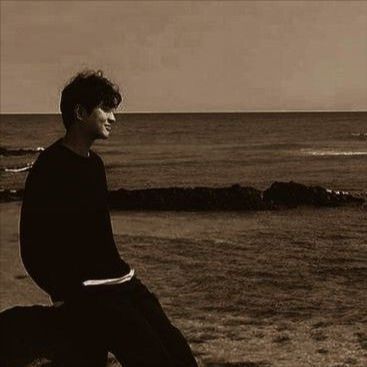 a man sitting on top of a rock next to the ocean