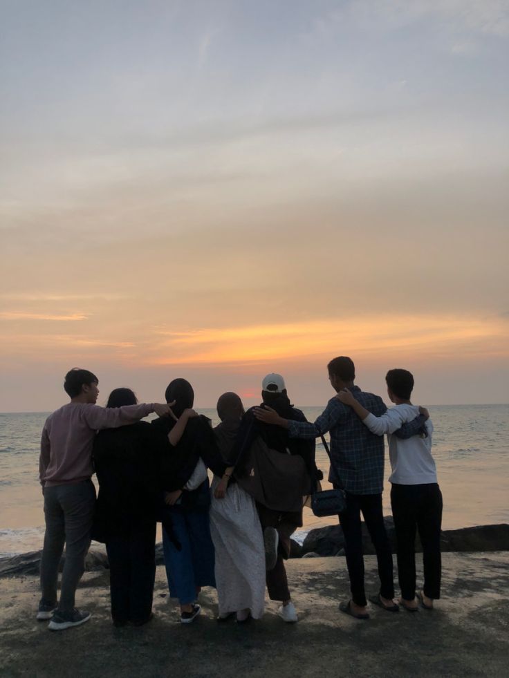 a group of people standing on top of a beach next to the ocean at sunset