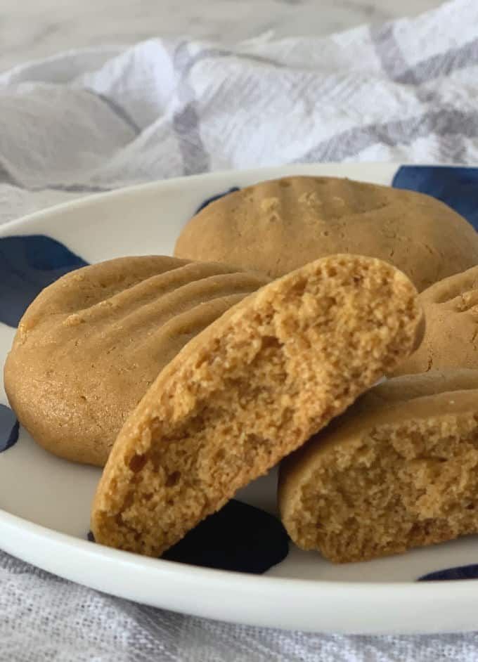 two peanut butter cookies on a plate with blue and white striped cloth behind them,