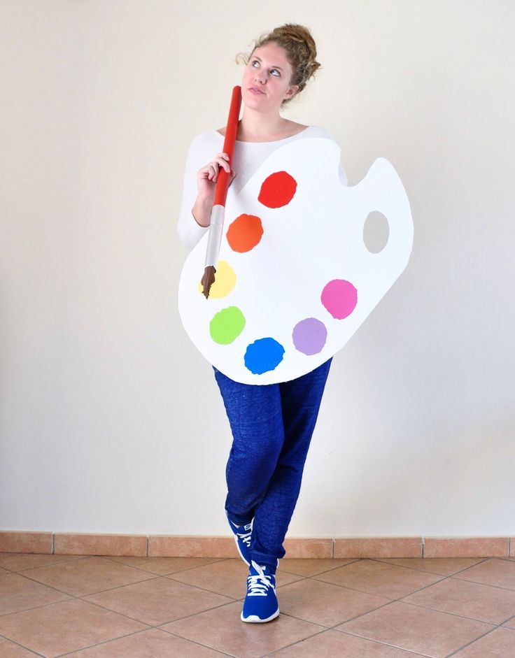 a woman holding a paint palette and a red pencil in her right hand while standing against a white wall