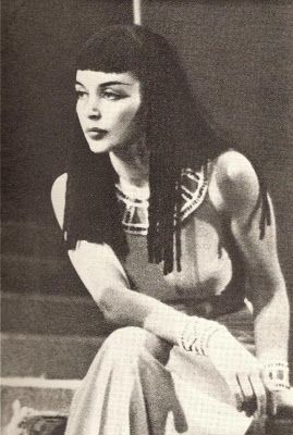 an old black and white photo of a woman with long hair sitting on the ground