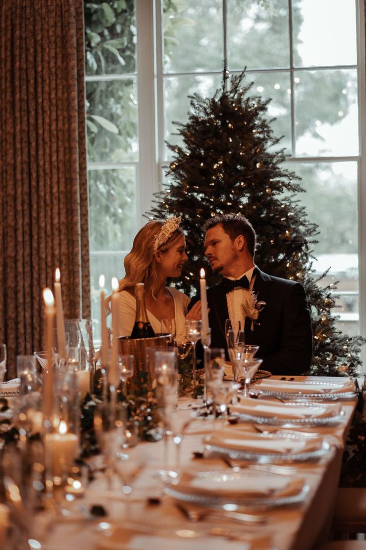 a man and woman sitting at a table in front of a christmas tree with lit candles