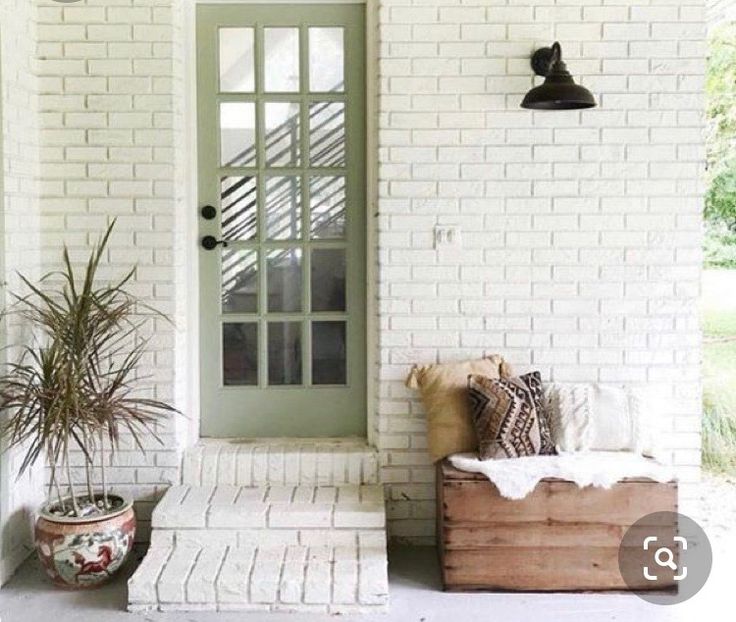 a white brick house with a green door and planter on the front porch area