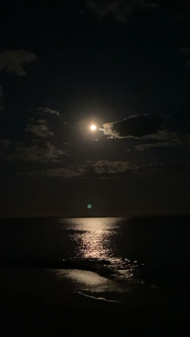 the moon is shining over the ocean at night with clouds in the sky and water