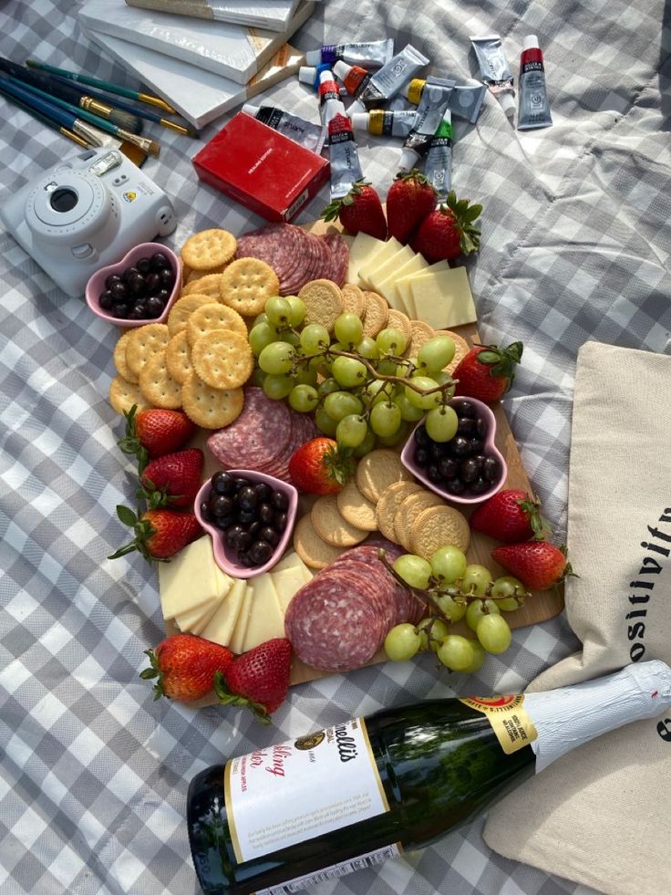 an assortment of cheeses, crackers, grapes and strawberries on a picnic blanket